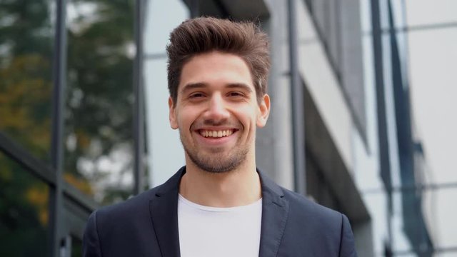 Smiling happy student man showing eureka gesture. Portrait of young thinking pondering businessman having idea moment pointing finger up on office building background