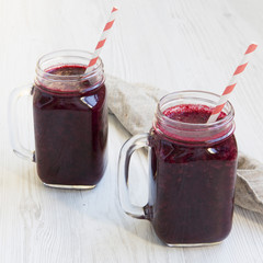 Glass jars with berry smoothie on white wooden background, side view. Close-up.