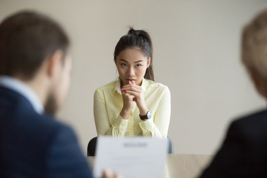 Nervous young Asian job applicant wait for recruiters question during interview in office, worried intern or trainee feel stressed applying for open position, meeting with hr managers. Hiring concept