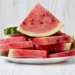 Chopped watermelon on a round white plate over white wooden background, close-up. Side view.