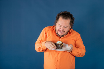 Funny fat man in orange shirt with a piece of chocolate cake on a plate