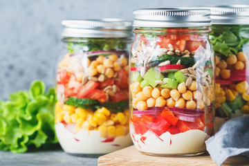 Fototapeta na wymiar Three glass jars with layering various vegan salads for healthy lunch. The concept of fitness and vegetarian food.