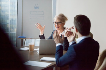 Colleagues congratulating middle aged female boss with high work achievement at meeting, employees...
