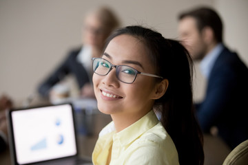 Portrait of smiling Asian female employee looking at camera during office business meeting, happy...