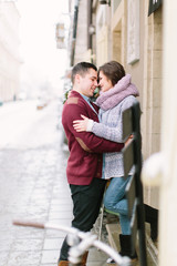 Fototapeta na wymiar Winter city love. Happy young couple in warm sweaters hugging near the building in winter city. Winter morning, christmas and holiday concept.
