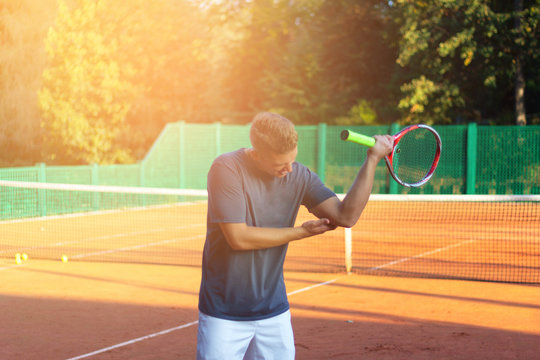 Handsome man on tennis court. Young tennis player. Pain in the elbow with sunlight in background
