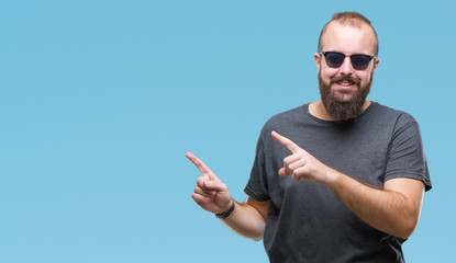 Young caucasian hipster man wearing sunglasses over isolated background smiling and looking at the camera pointing with two hands and fingers to the side.