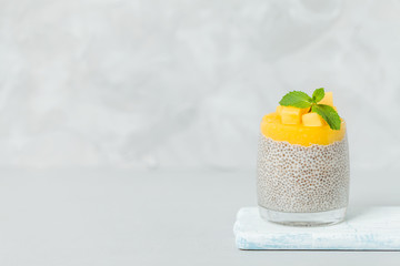 Fototapeta na wymiar Chia seeds pudding with mango puree in beautiful glasses with green mint leaves and cut fresh ripe tropical fruit.