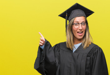 Young beautiful woman wearing graduated uniform over isolated background with a big smile on face, pointing with hand and finger to the side looking at the camera.