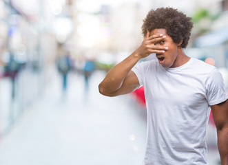 Afro american man over isolated background peeking in shock covering face and eyes with hand, looking through fingers with embarrassed expression.