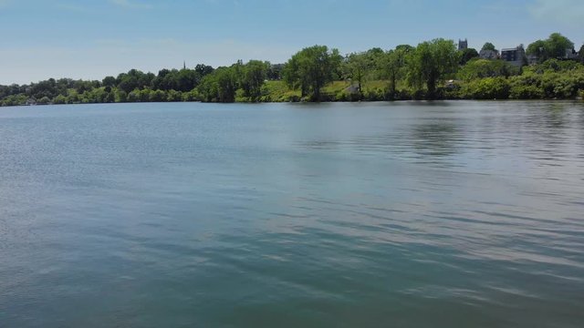 Aerial Fly Over Water Toward Tree Shore. an aerial view flying over calm water in a lake toward the treeline shore