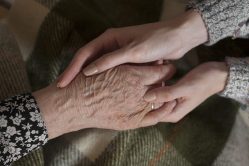 Young woman hands are holding an elderly woman hand; people, care and love concept.