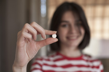Girl is showing a pill; focus on hand with the pill; people and health concept.