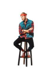 stylish man in denim vest and red checkered shirt sitting on chair with crossed arms isolated on white