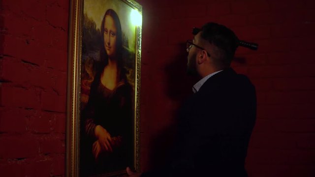 Young man with glasses a thief looks over Mona Lisa Portrait with a flashlight in his hands before stealing a masterpiece