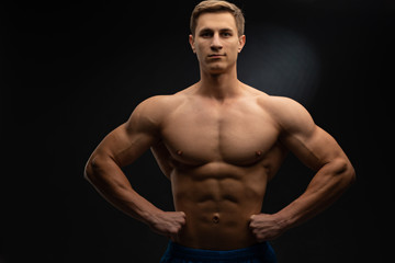 Fototapeta na wymiar young, Strong bodybuilder with six packs. Bodybuilder flexes muscles against dark background
