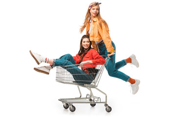 beautiful hipster girl carrying shopping cart with smiling female friend isolated on white © LIGHTFIELD STUDIOS