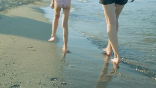 Woman with daughter walking along coast in summer day