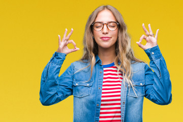 Beautiful young blonde woman wearing glasses over isolated background relax and smiling with eyes closed doing meditation gesture with fingers. Yoga concept.