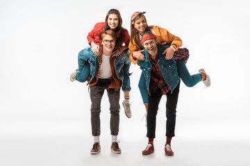 cheerful stylish hipsters doing piggyback ride to their smiling girlfriends isolated on white