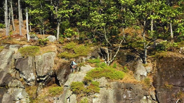 Aerial footage ORBIT around lone climber at the top of a cliff in Maine