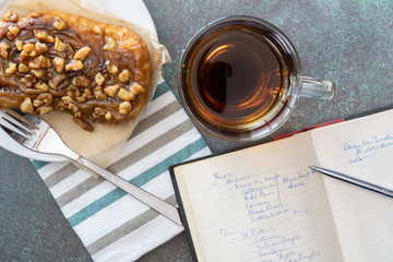 travel planning diary and pen with dessert of a sticky bun with walnuts on a white plate with fork and striped napkin and a cup of coffee