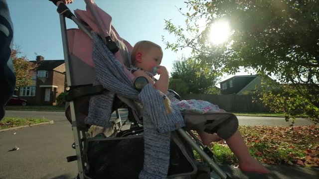 Slow motion steady cam view of a Caucasian toddler in a pram backlit by the sun