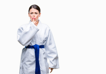 Young beautiful woman wearing karate kimono uniform over isolated background asking to be quiet with finger on lips. Silence and secret concept.