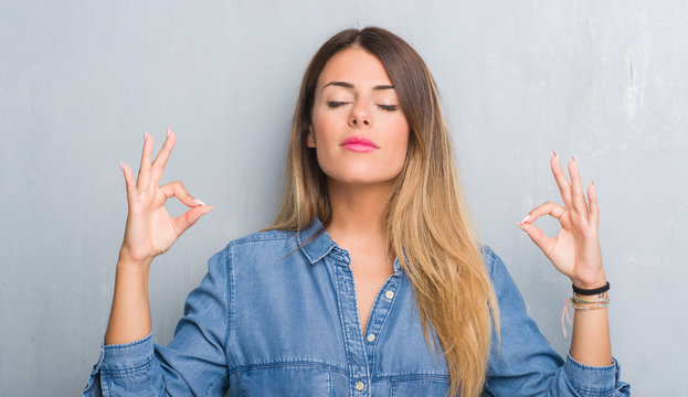 Young adult woman over grunge grey wall wearing denim outfit relax and smiling with eyes closed doing meditation gesture with fingers. Yoga concept.