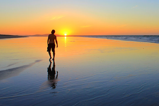 Young man walking on the beach at sunset time