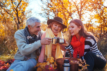 Senior parents drinking tea in autumn forest with their daughter. Family values. Having picnic