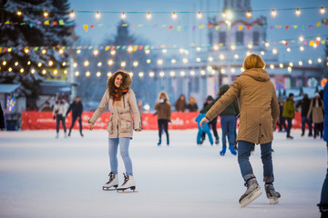 Obraz premium Young couple in love Caucasian man with blond hair with long hair and beard and beautiful woman have fun, active date skating on ice scene in town square in winter on Christmas Eve