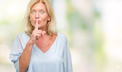 Middle age blonde business woman over isolated background asking to be quiet with finger on lips....