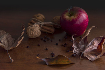 Single apple and dried leaves on a wooden table, close up
