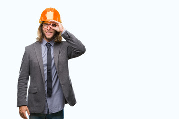 Young handsome architec man with long hair wearing safety helmet over isolated background doing ok gesture with hand smiling, eye looking through fingers with happy face.