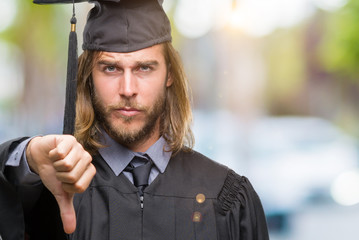 Young handsome graduated man with long hair over isolated background looking unhappy and angry showing rejection and negative with thumbs down gesture. Bad expression.