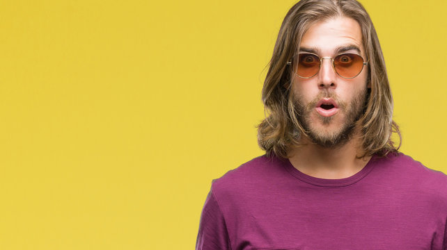Young handsome man with long hair wearing sunglasses over isolated background afraid and shocked with surprise expression, fear and excited face.