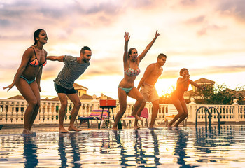 Group of happy friends jumping in the pool at sunset - Young people having fun making party in exclusive resort tropical in vacation - Concept of friendship, holidays and youth lifestyle - obrazy, fototapety, plakaty