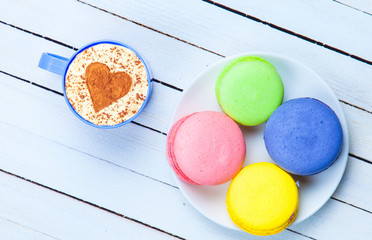 Cup of Cappuccino with heart shape symbol and macaron on white wooden background