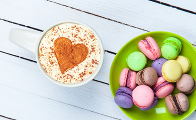 Cup of Cappuccino with heart shape symbol and macaron on white wooden background