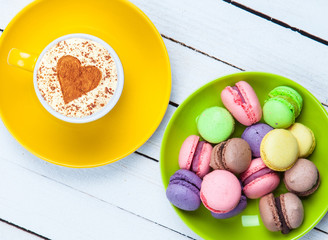 Cup of Cappuccino with heart shape symbol and macaron on white wooden background