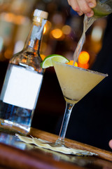 Martini drink and limes on bar with blank bottle, bartender, and bokeh