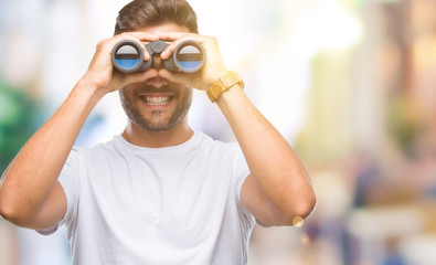 Young handsome man looking through binoculars over isolated background with a happy face standing...