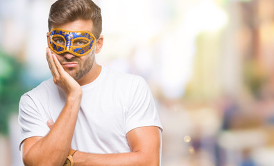 Young handsome man wearing carnival mask over isolated background thinking looking tired and bored...