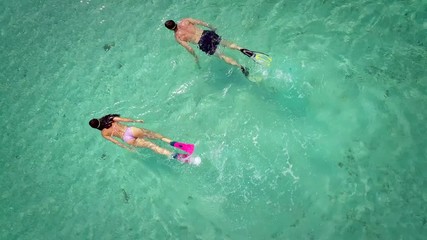 Close up aerial view of man and woman snorkeling with masks and flippers in transparent turquoise sea.