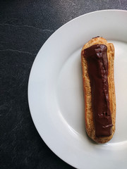 éclair au chocolat vu de haut sur une assiette blanche et un fond gris