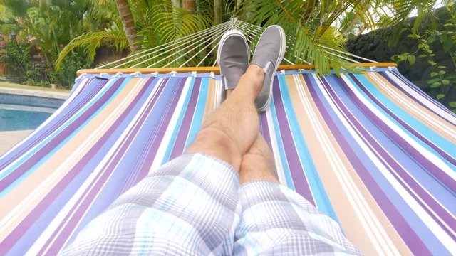 Hammock Swing Point of View Tlit Up. a slow motion personal point of view of a male swinging on a hammock, tilt up from legs on hammock to palm trees