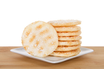 Pile of Japanese rice crackers on a small white square porcelain plate on wood table isolated behind. Rice crackers are usually low in sugar and fat.