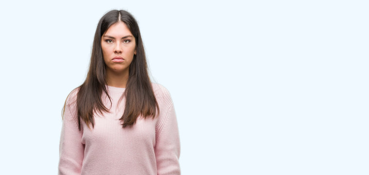 Young beautiful hispanic woman wearing a sweater with serious expression on face. Simple and natural looking at the camera.