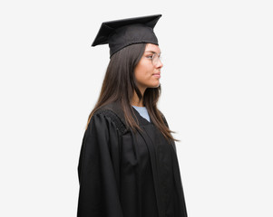 Young hispanic woman wearing graduated cap and uniform looking to side, relax profile pose with...